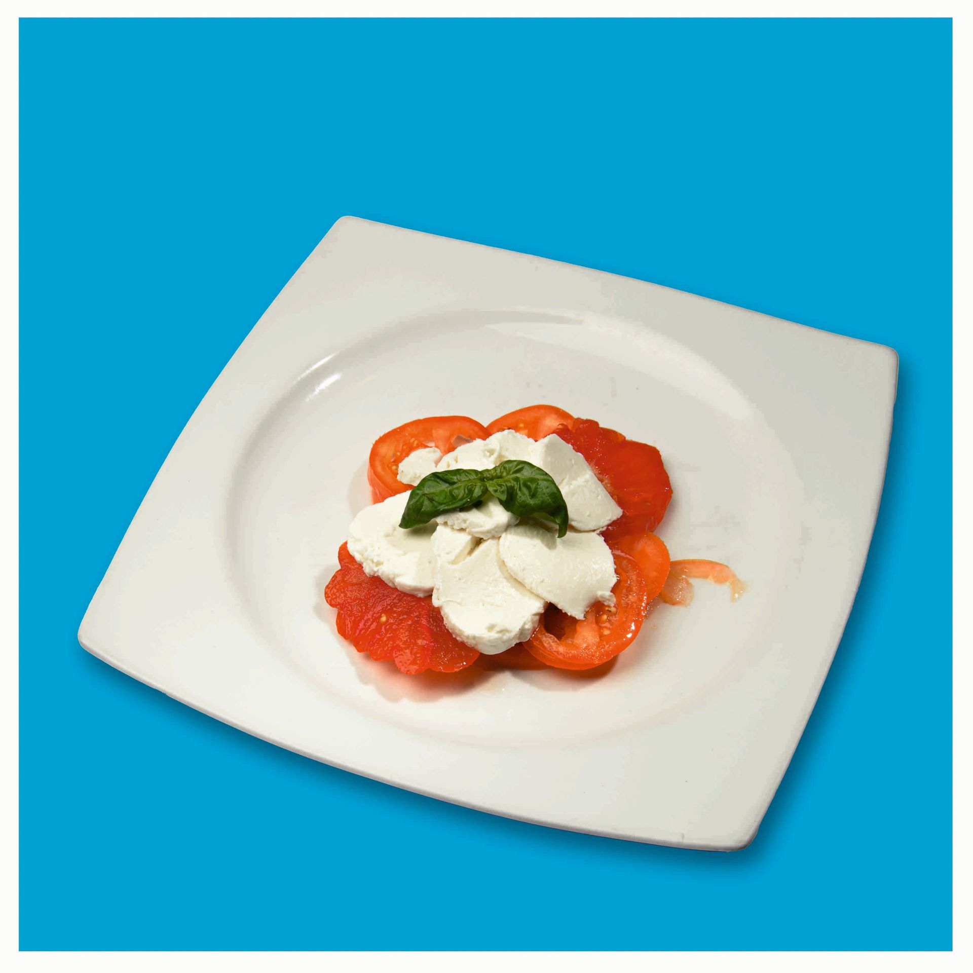 Un piatto bianco con pomodori e mozzarella su uno sfondo blu