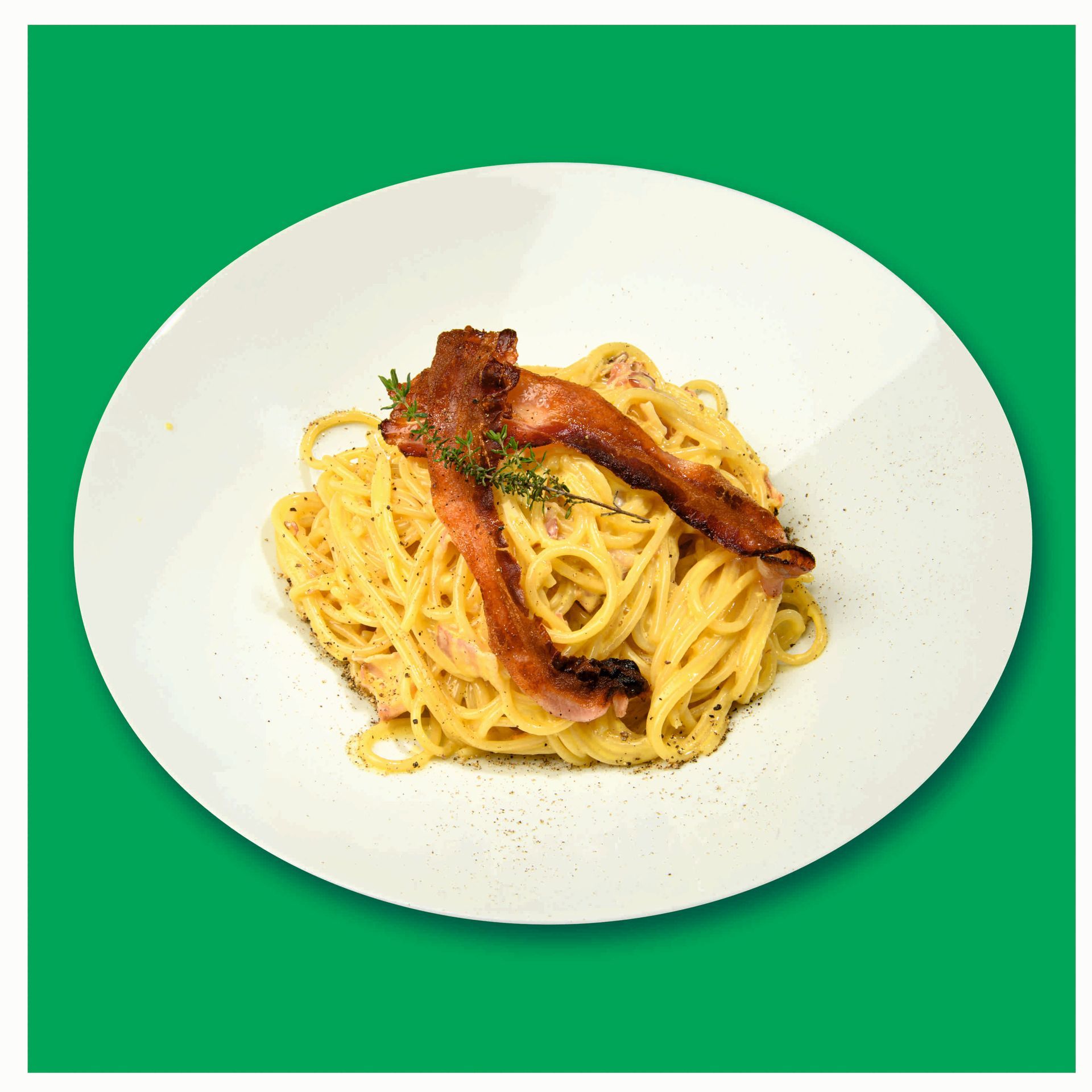 Un piatto bianco con sopra spaghetti e pancetta su uno sfondo verde.