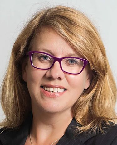 A woman wearing purple glasses and a black jacket is smiling.