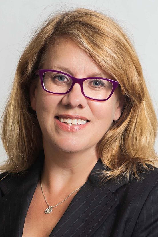 A woman wearing glasses and a necklace is smiling for the camera.