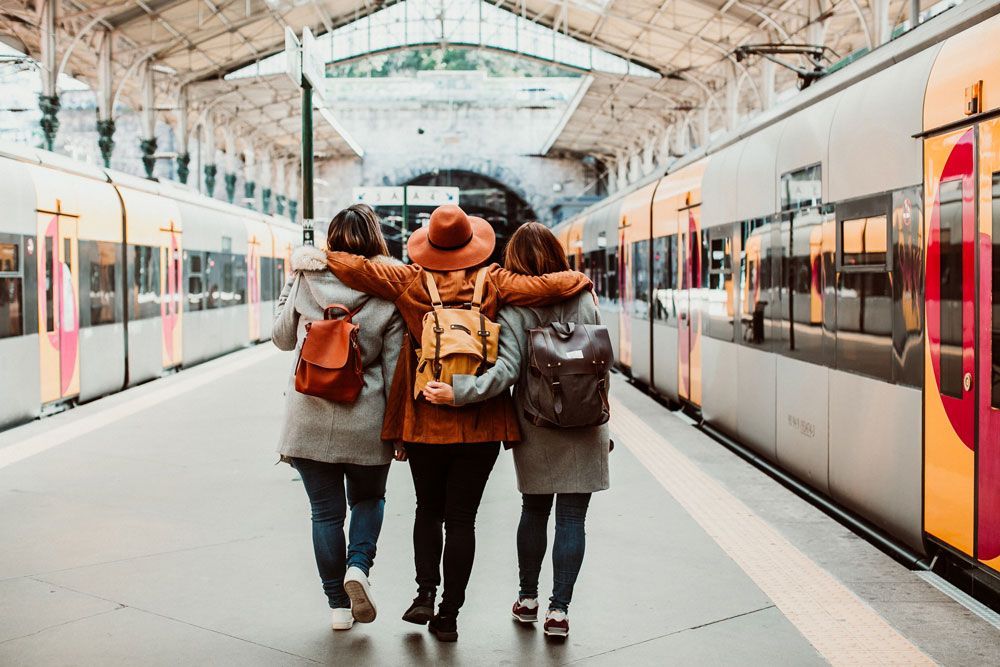 Three friends with arms around each other, walking on a train platform. Trains on either side.