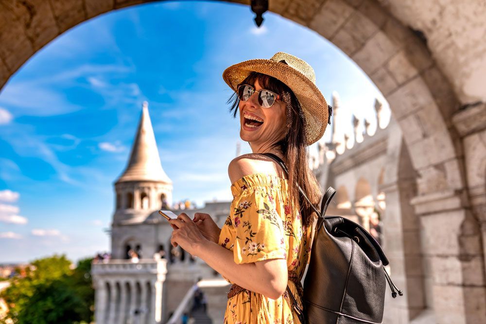 Woman with straw hat smiles at camera; Budapest castle in background.