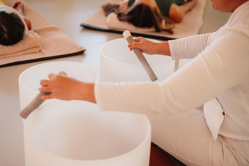 Person playing crystal singing bowls during a sound bath session.