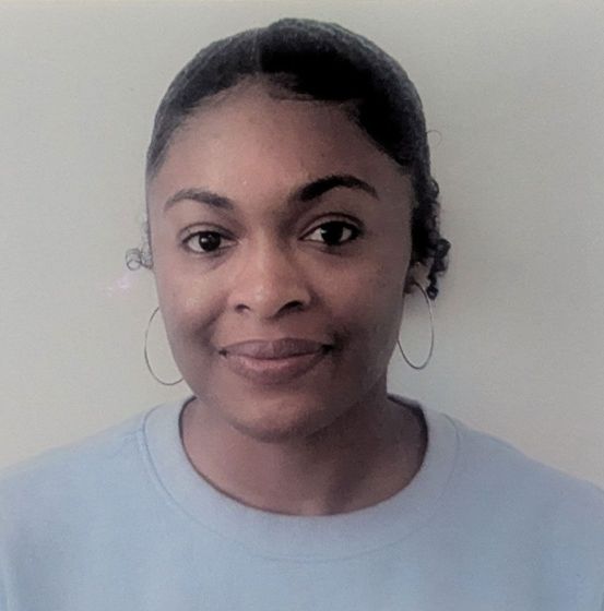 A woman wearing a light blue sweater and hoop earrings is smiling for the camera.