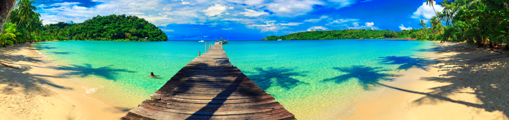 Beach scene with wooden pier, turquoise water, and lush green islands under a blue sky.