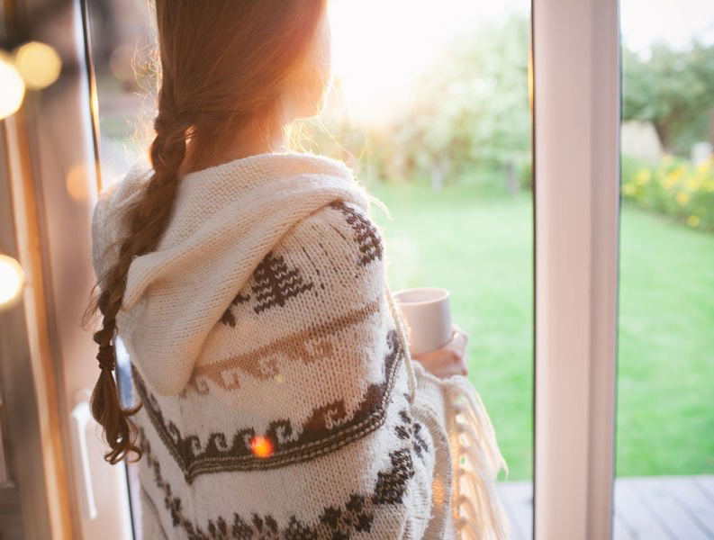 A woman is standing in front of a window holding a cup of coffee.