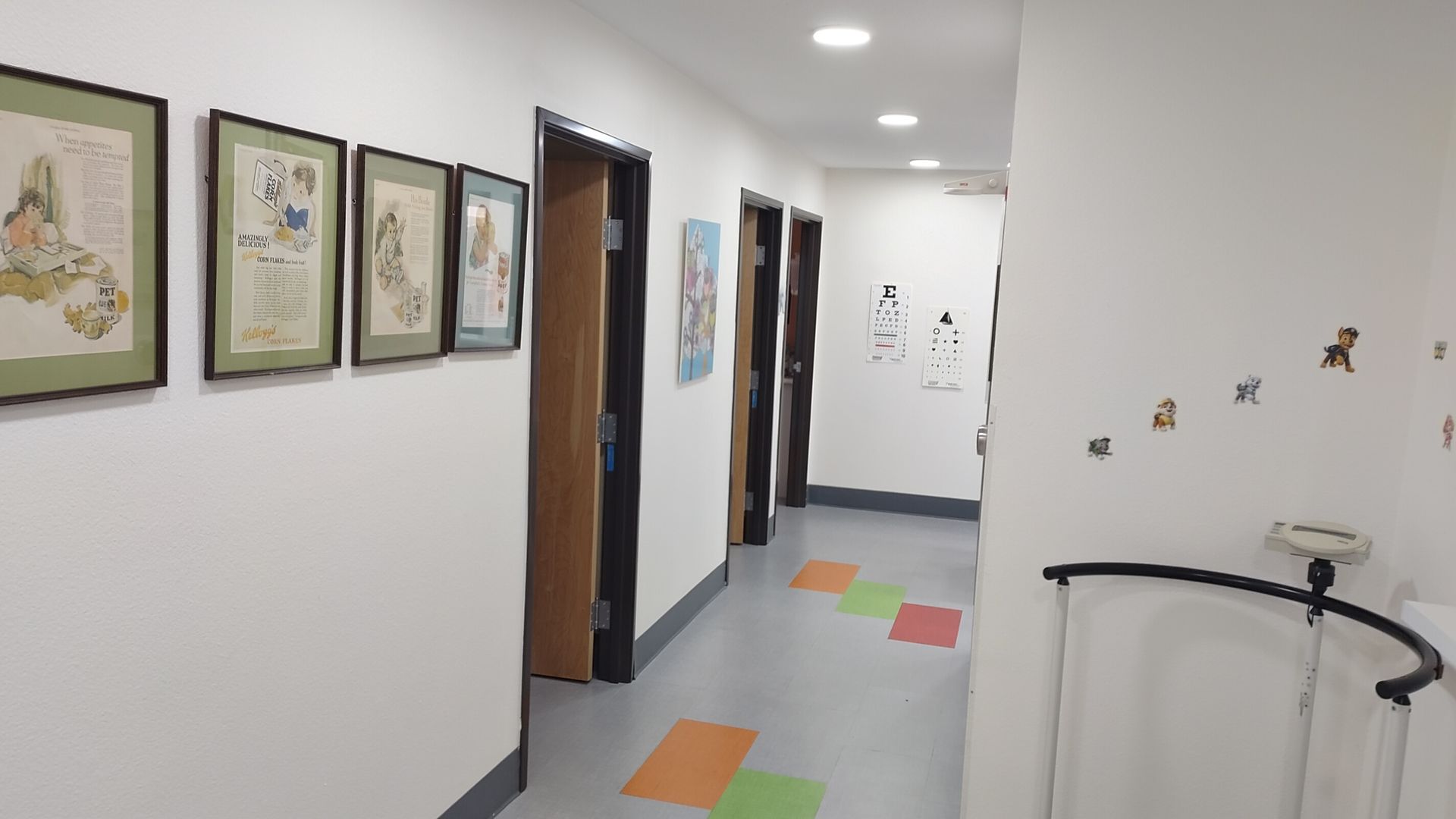 A long hallway with a lot of doors and paintings on the wall.