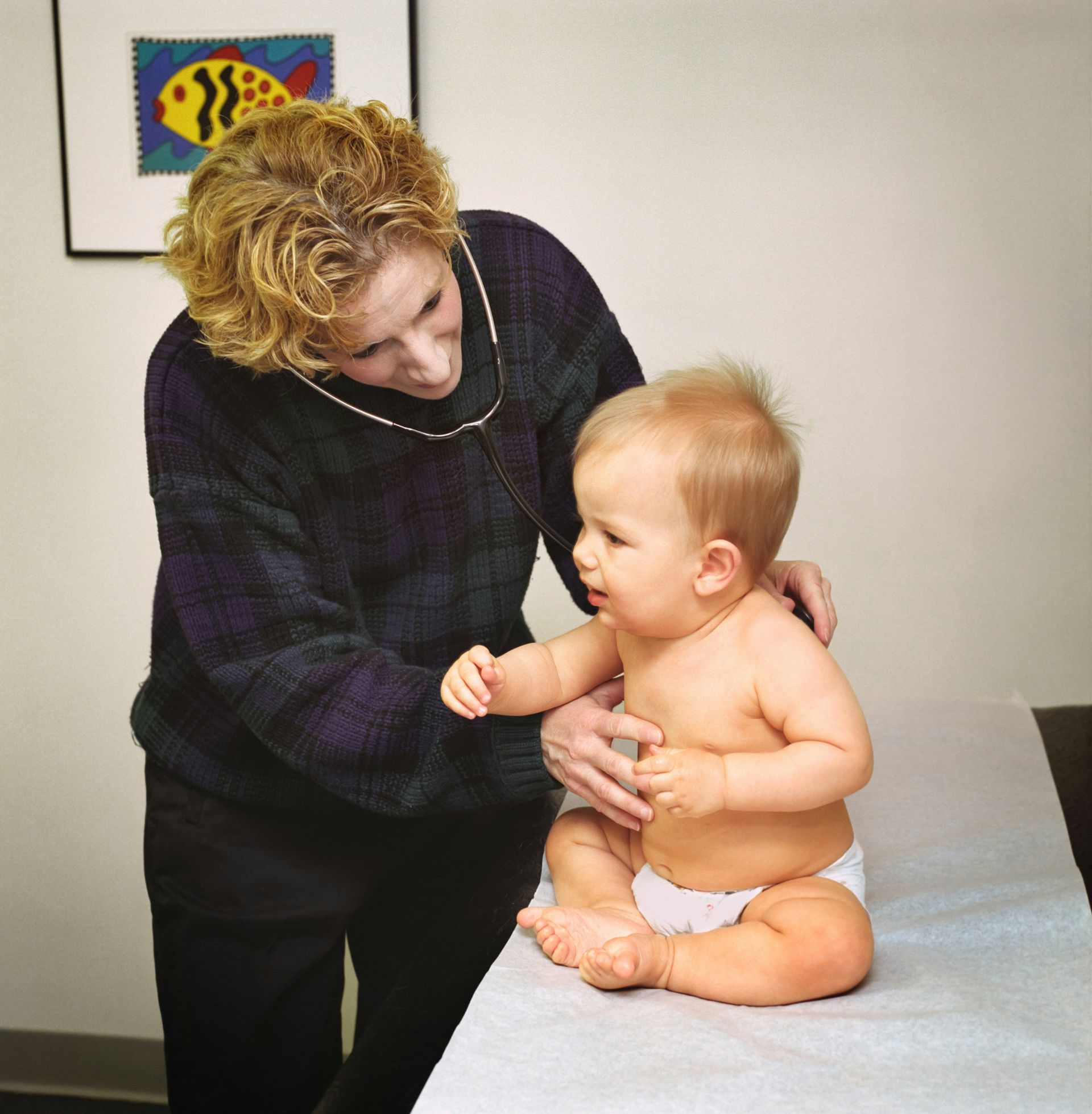 A woman examines a baby on a table with a picture of a fish on the wall behind her