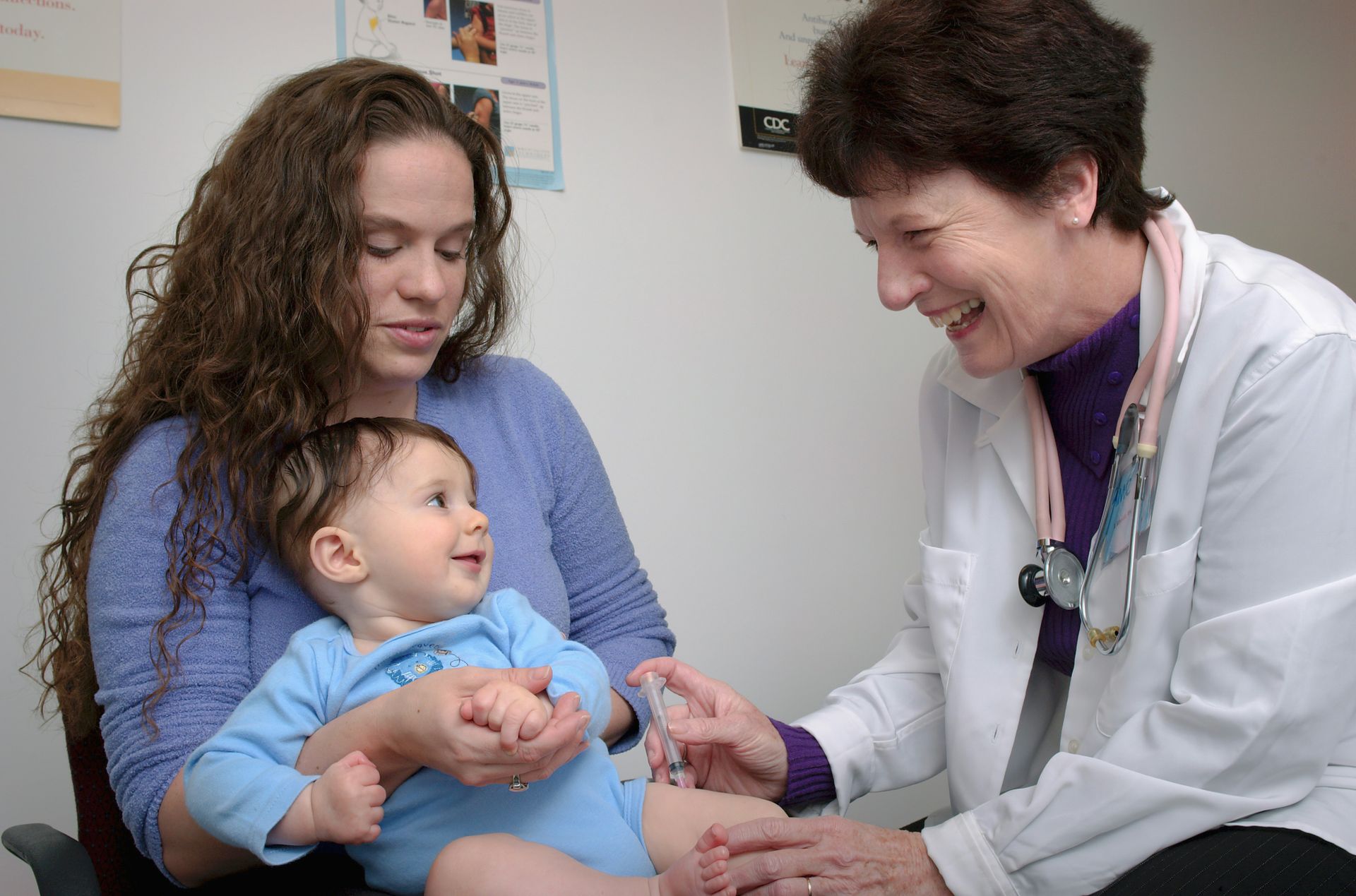 A woman is holding a baby while a doctor gives it an injection