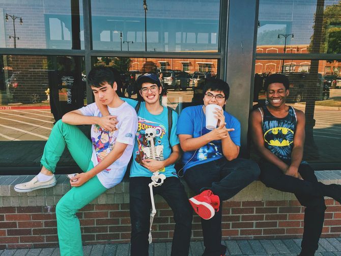 A group of young men are sitting on a brick wall drinking milkshakes