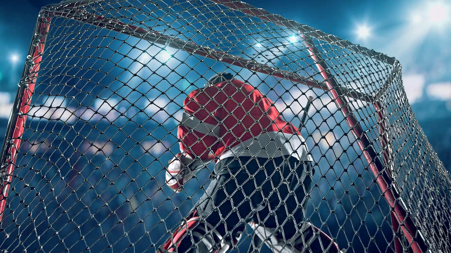 A hockey goalie is standing in front of a net holding a hockey stick.