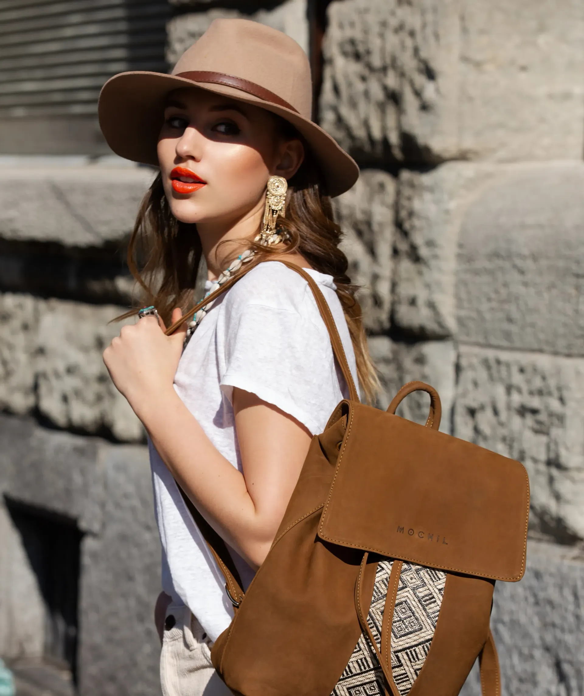 Frau mit orangerotem Lippenstift trΓ€gt Hut und stylischen Rucksack einer schweizer Marke