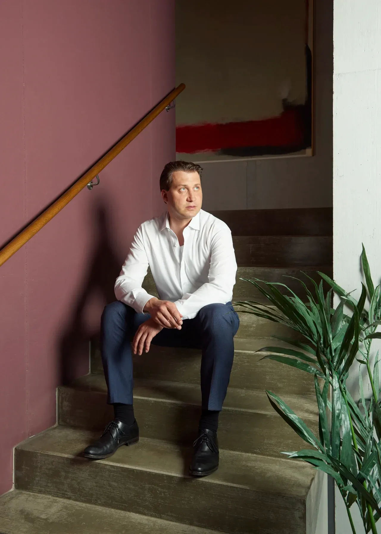 Firmeninhaberportrait in Anzug auf Treppe sitzend, nachdenklicher Blick