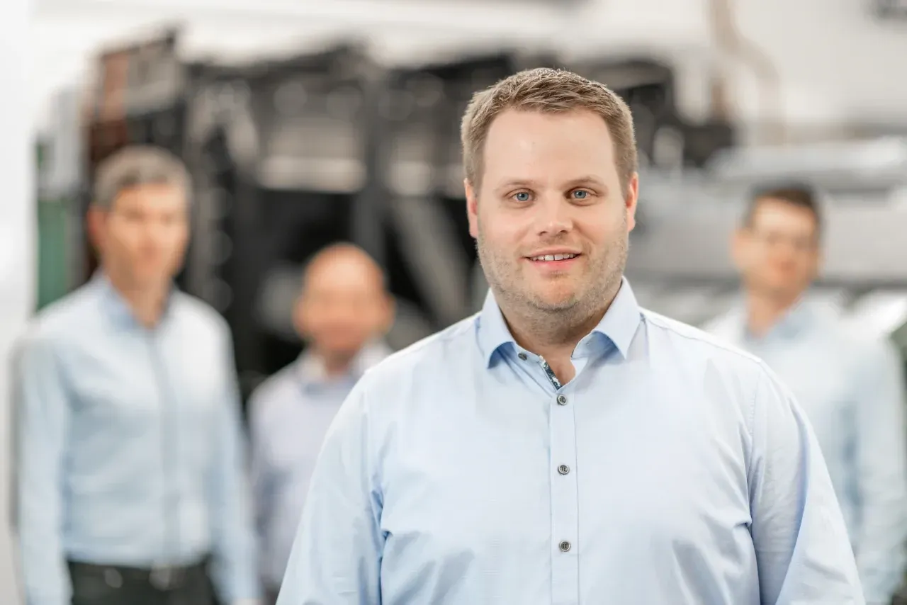 Mitarbeiterportrait mit Fokus auf Person im Vordergrund, Mitarbeiter im Hintergrund unscharf