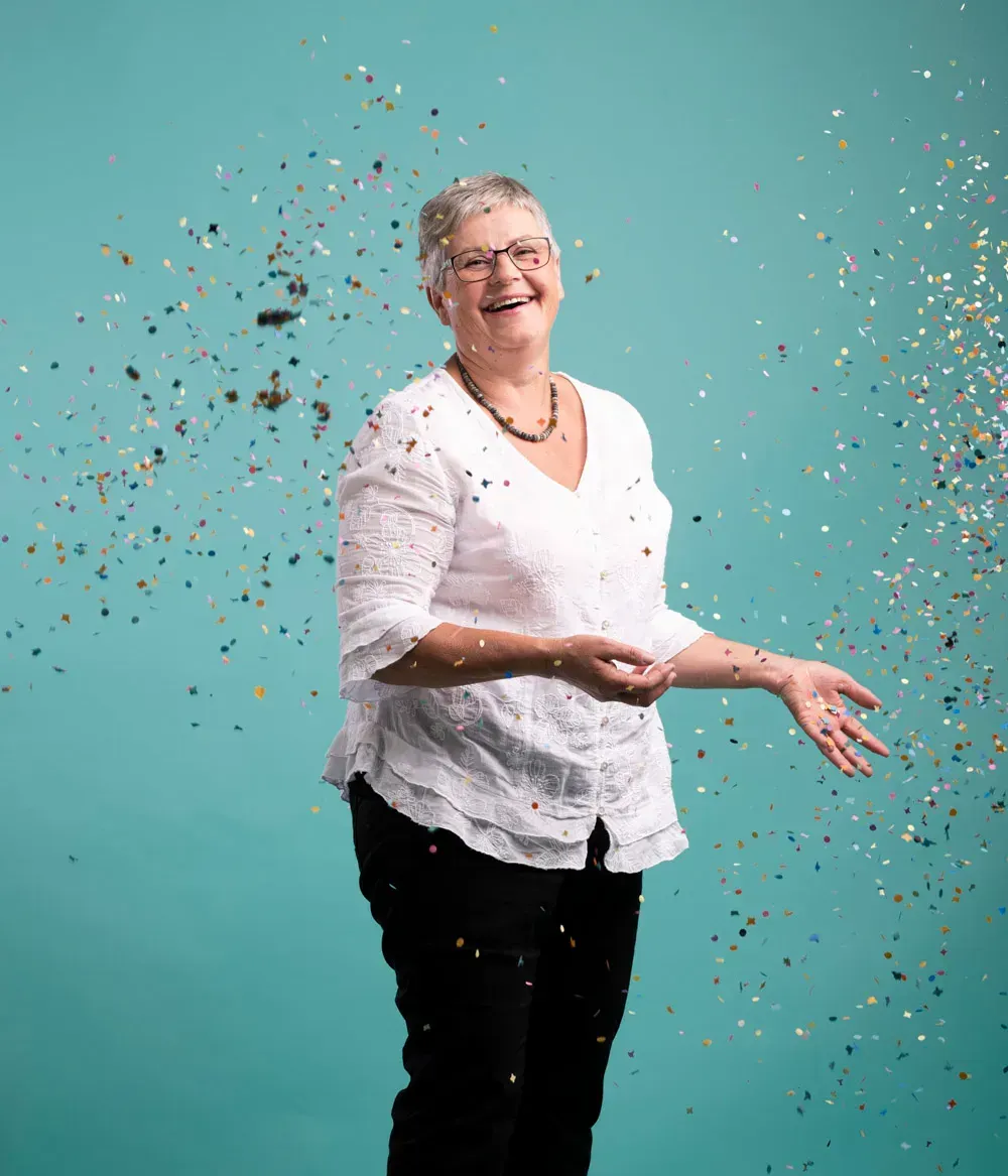 natuerliches makeup an aelterer lachender dame fΓΌr fotoshooting mit brille und konfetti