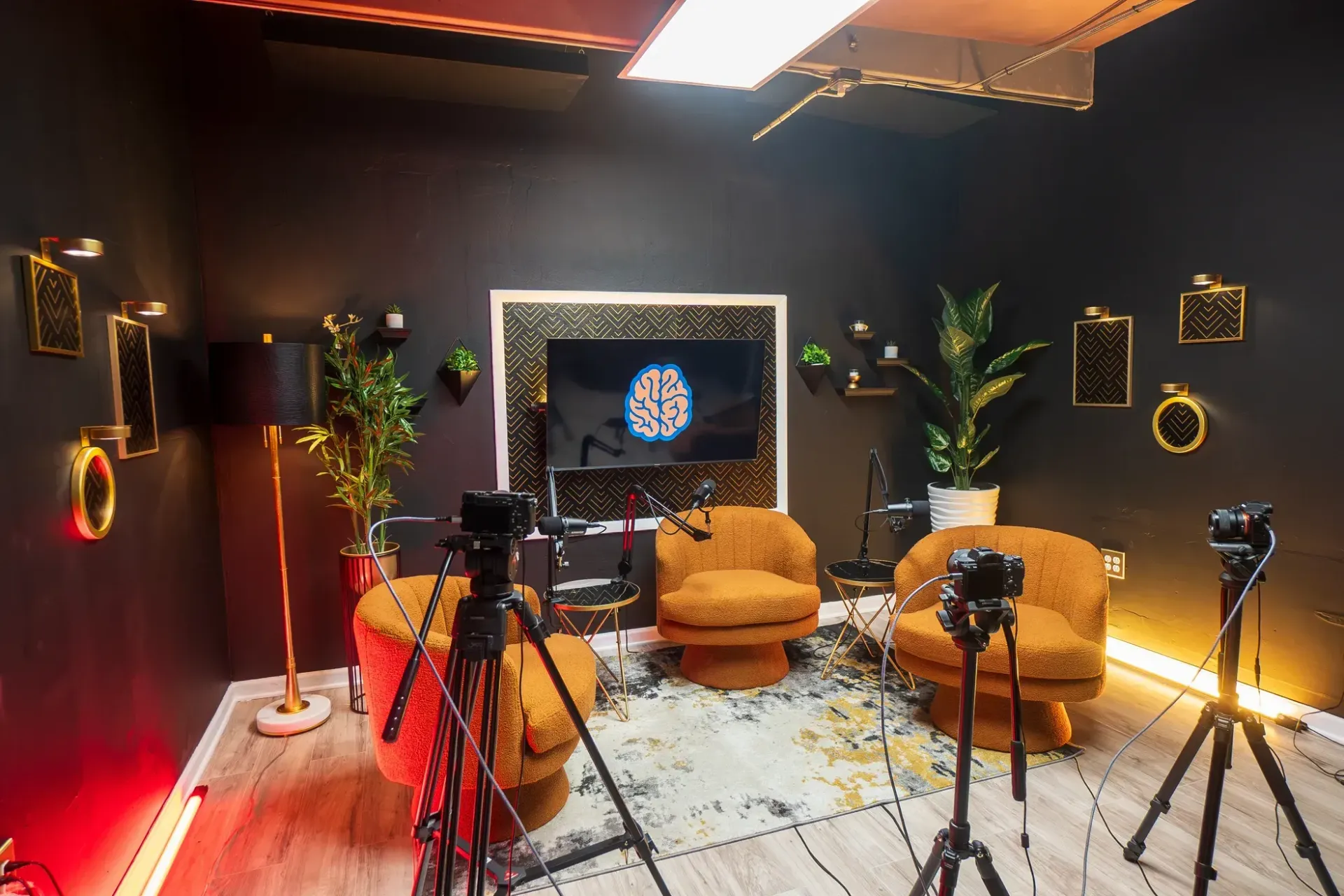 Podcast studio with orange chairs, black walls, and cameras set up for recording.