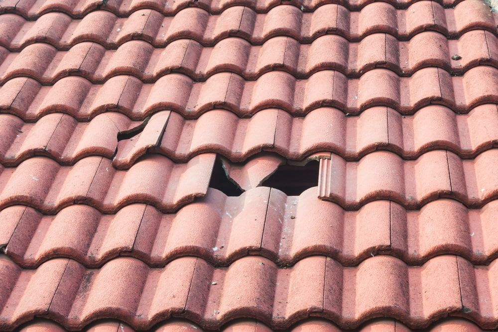 Damaged red tile roof with a large hole. — Lee Pakau Roofing & Guttering in Murwillumbah, NSW