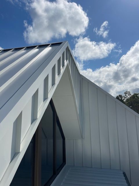White metal roof with rectangular cutouts against a blue sky with fluffy clouds. — Lee Pakau Roofing & Guttering in Banora Point, NSW