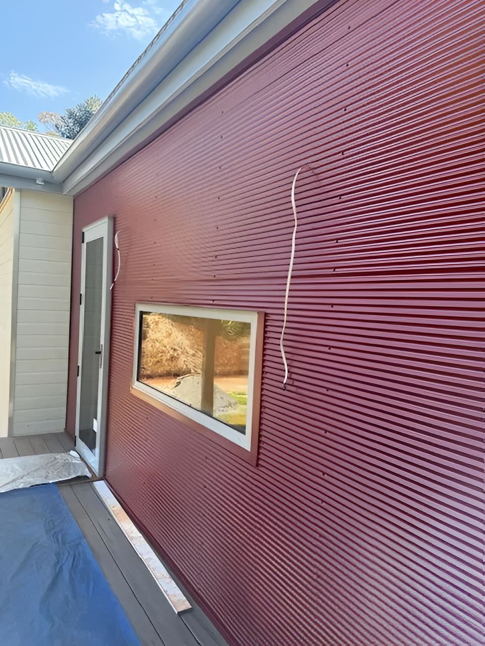 Red corrugated metal building exterior with a door and window. White trim and gutter. — Lee Pakau Roofing & Guttering in Banora Point, NSW
