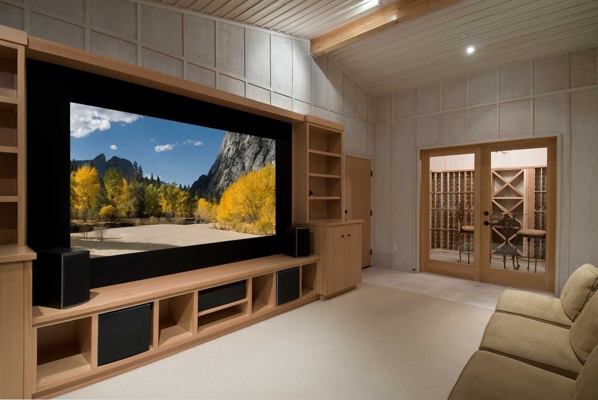Home theater with large screen, wooden cabinets, and sofa; glass doors lead to a wine cellar.