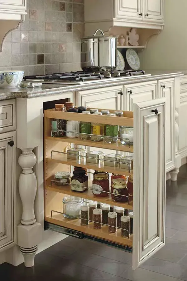 Pull-out spice rack in a white kitchen cabinet, with jars of spices on wooden shelves.