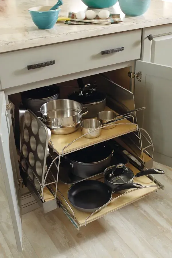 Pull-out kitchen cabinet with pans and baking tins, gray cabinets, light countertops, interior storage.