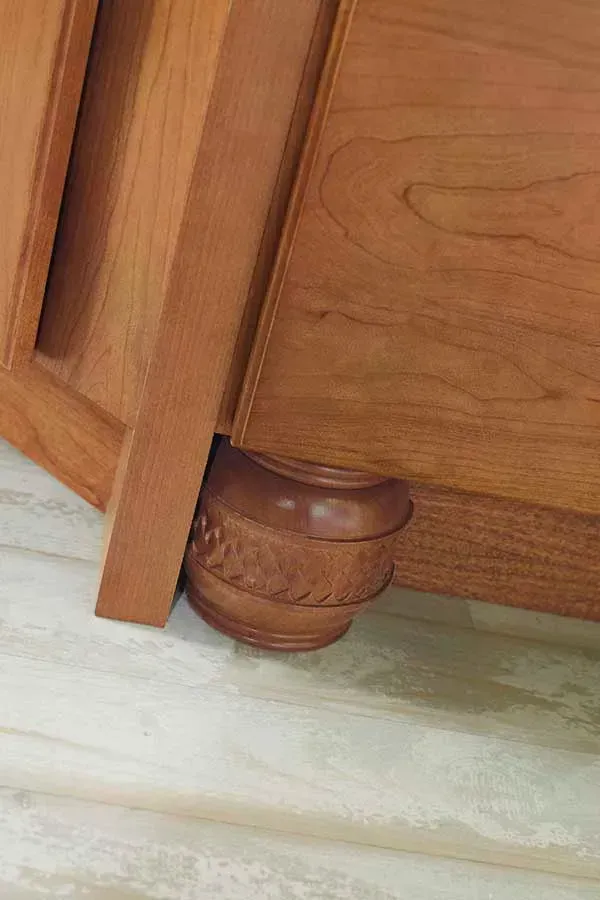 Wooden furniture corner with carved decorative foot resting on a light-colored floor.