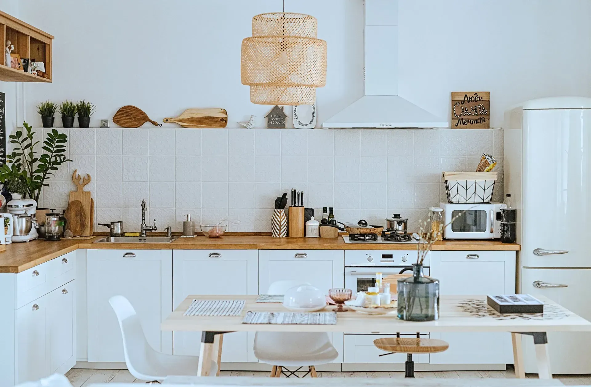 Bright, airy kitchen with white cabinets, light wood counters, and a decorative woven light fixture.