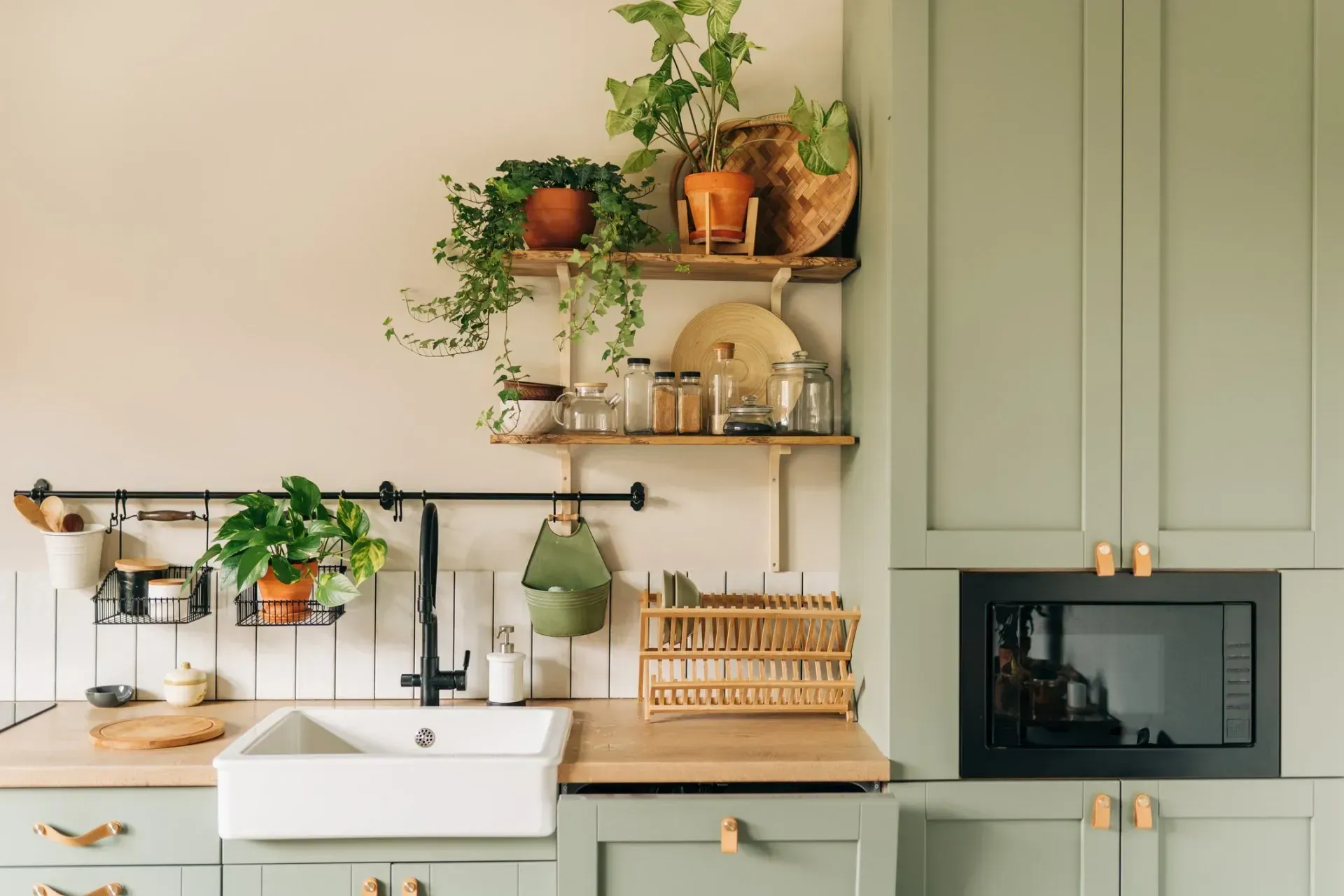 A kitchen with sage green cabinets, plants on shelves, and a built-in microwave.