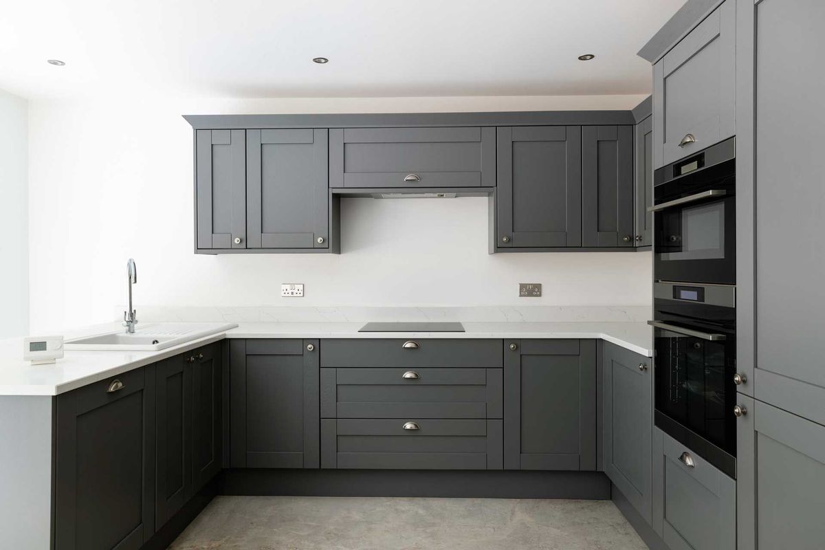 Grey kitchen cabinets with white countertop, stainless steel sink and oven.