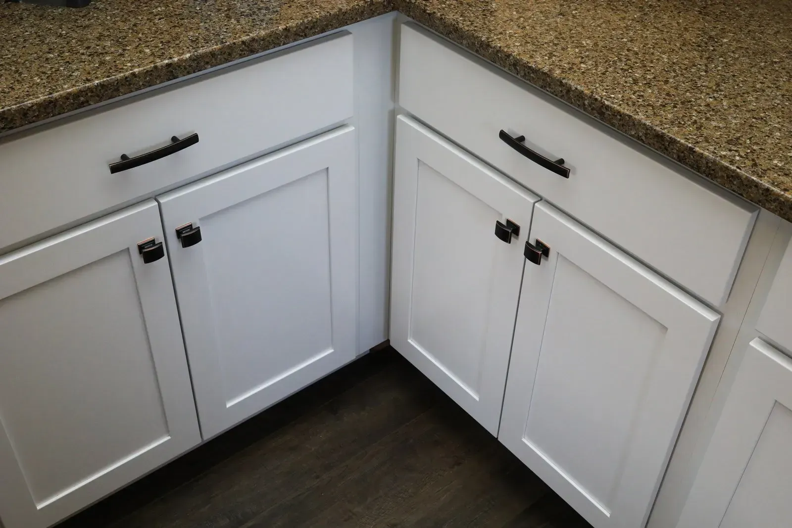 White kitchen cabinets with black hardware under a brown speckled countertop.