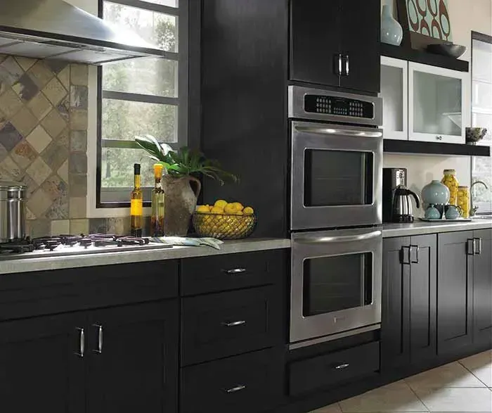 Dark kitchen with black cabinets, stainless steel oven, and window.
