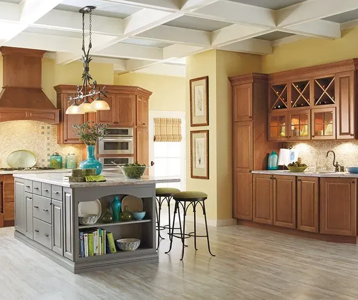 Kitchen with wooden cabinets, gray island, marble countertops, and yellow walls.