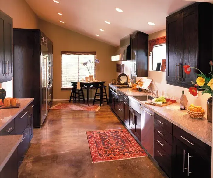 Dark brown kitchen with stainless steel appliances, tan walls, and area rugs.