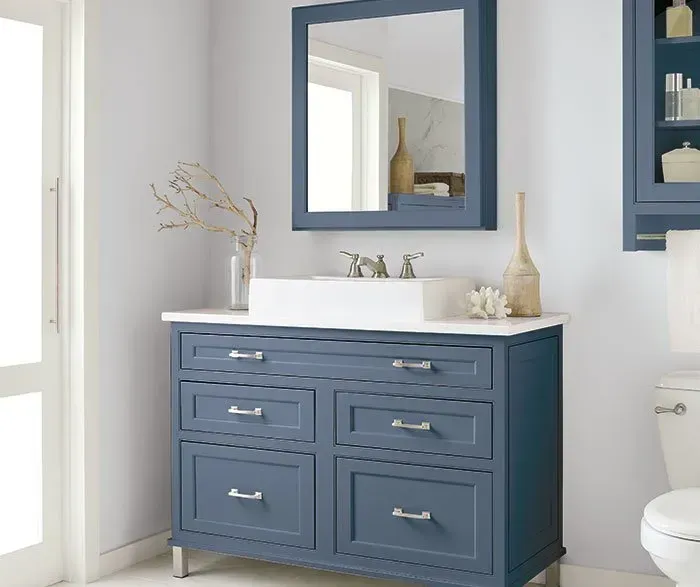 Blue bathroom vanity with a white countertop, rectangular mirror, and light-colored walls.