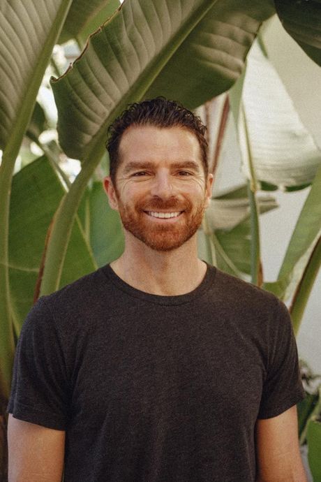 A man with a beard is smiling in front of a palm tree.