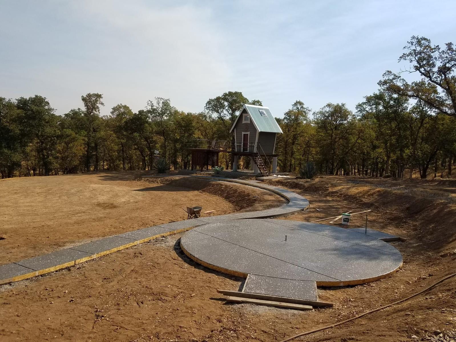 A house is being built in the middle of a dirt field surrounded by trees.