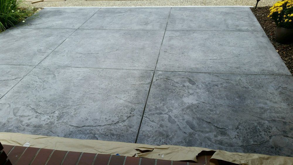 A concrete driveway with a brick wall and flowers in the background.