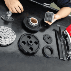 Mãos exibindo peças de motor: engrenagens, rodas dentadas, corrente de distribuição e componentes relacionados, dispostos sobre uma superfície escura.