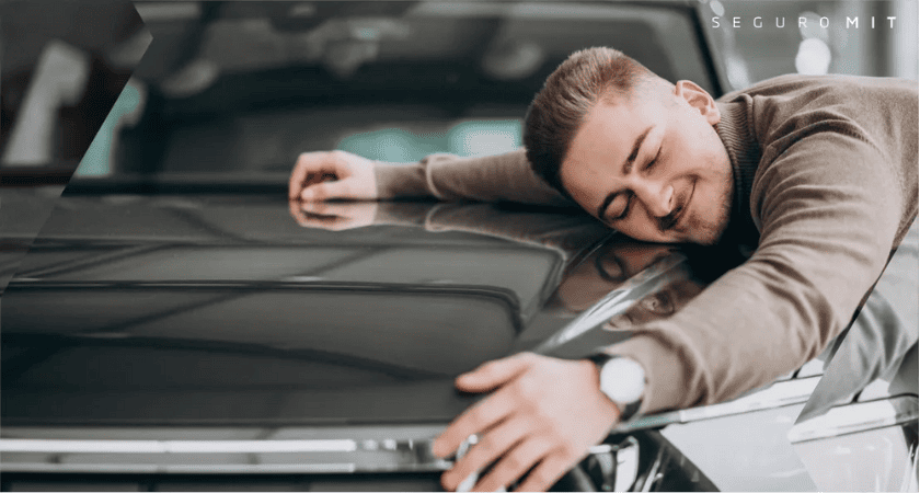 Homem com a cabeça apoiada no capô de um carro, sorrindo e usando um relógio de pulso.