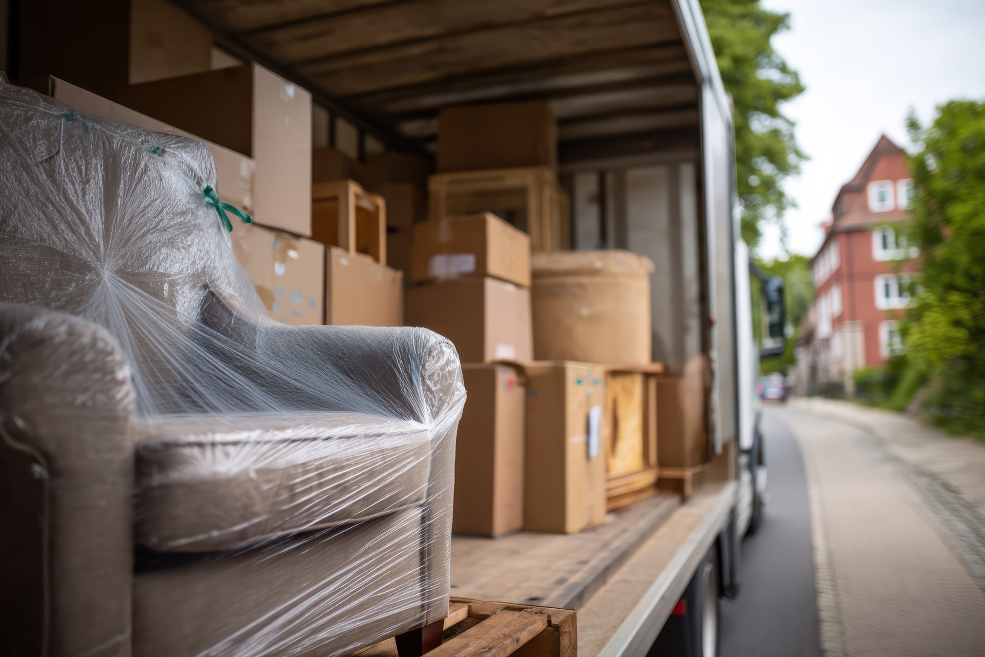 Moving truck loaded with furniture and boxes on a residential street. An armchair is wrapped in plastic.