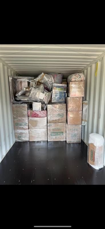 Boxes and wrapped items fill a shipping container, with one standing item in front.