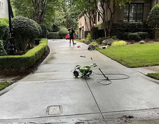 A drone is sitting on the side of a concrete driveway next to a house.