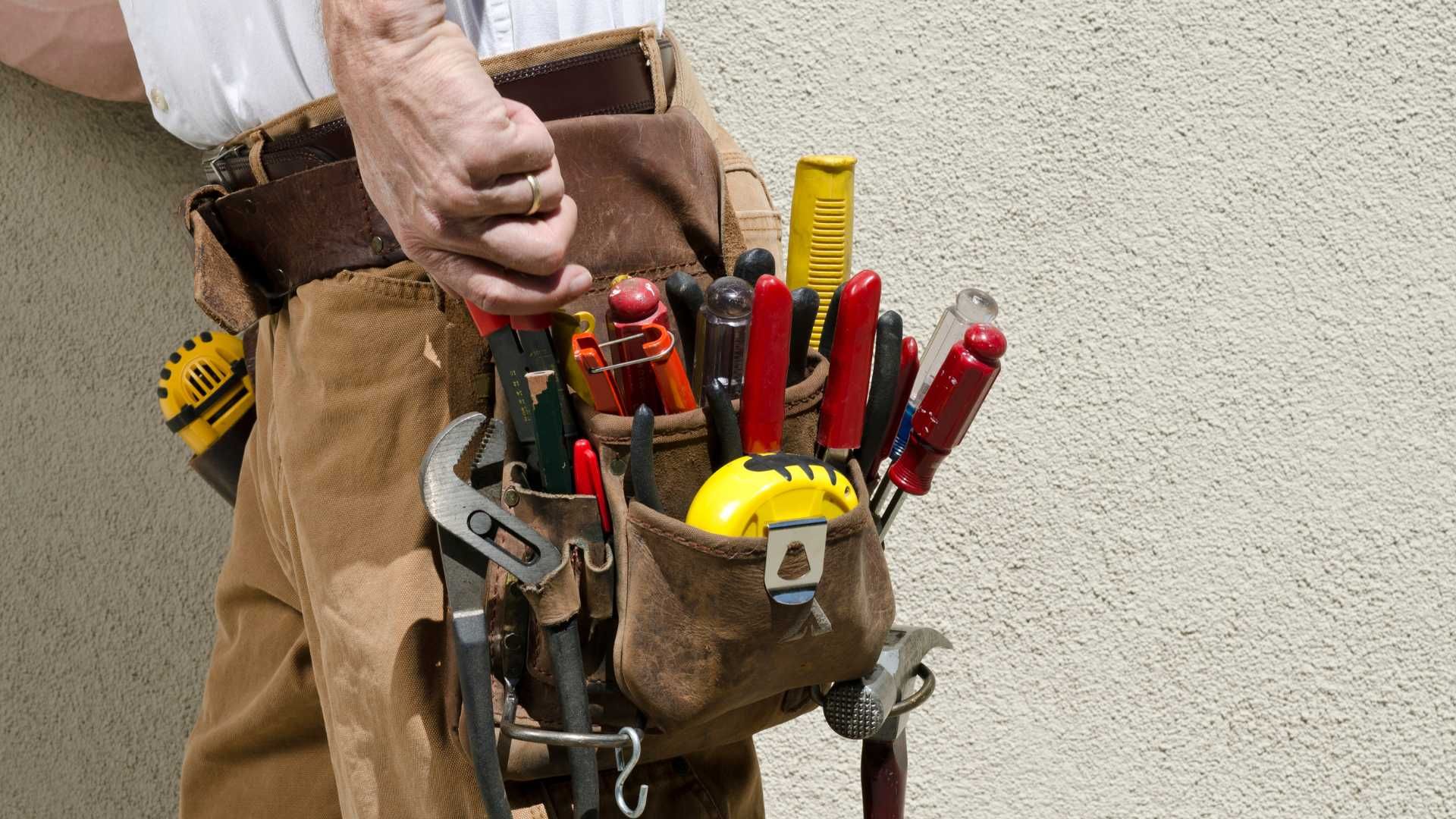 A man is holding a tool belt full of tools.