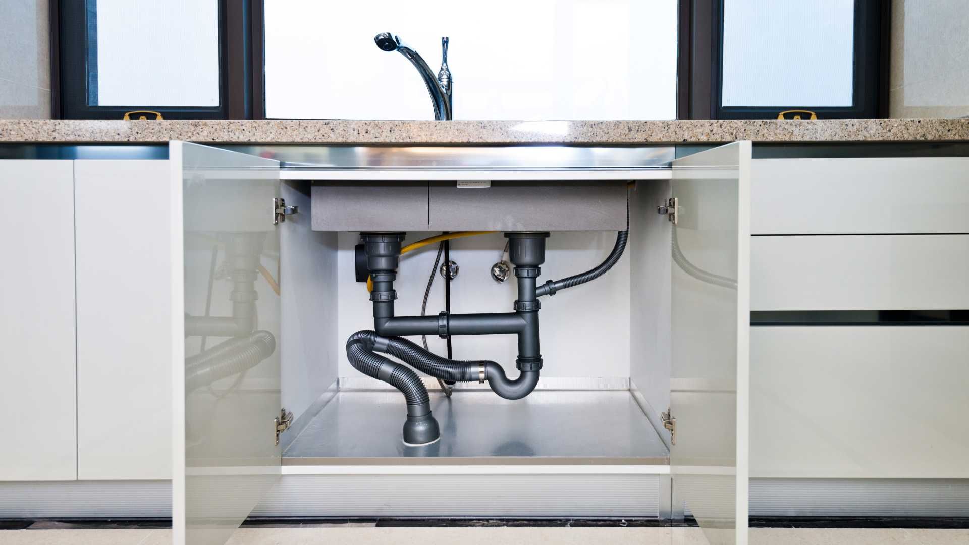 A kitchen sink is under a cabinet with the doors open.