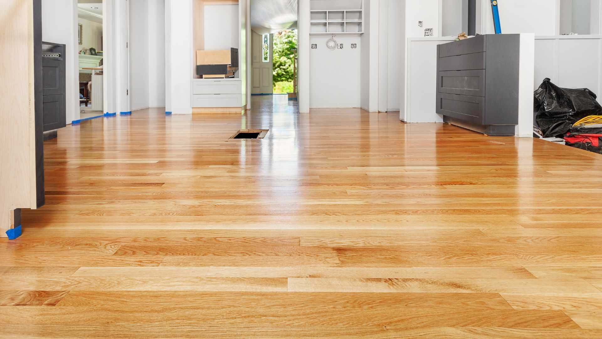 A living room with a wooden floor and a kitchen in the background.