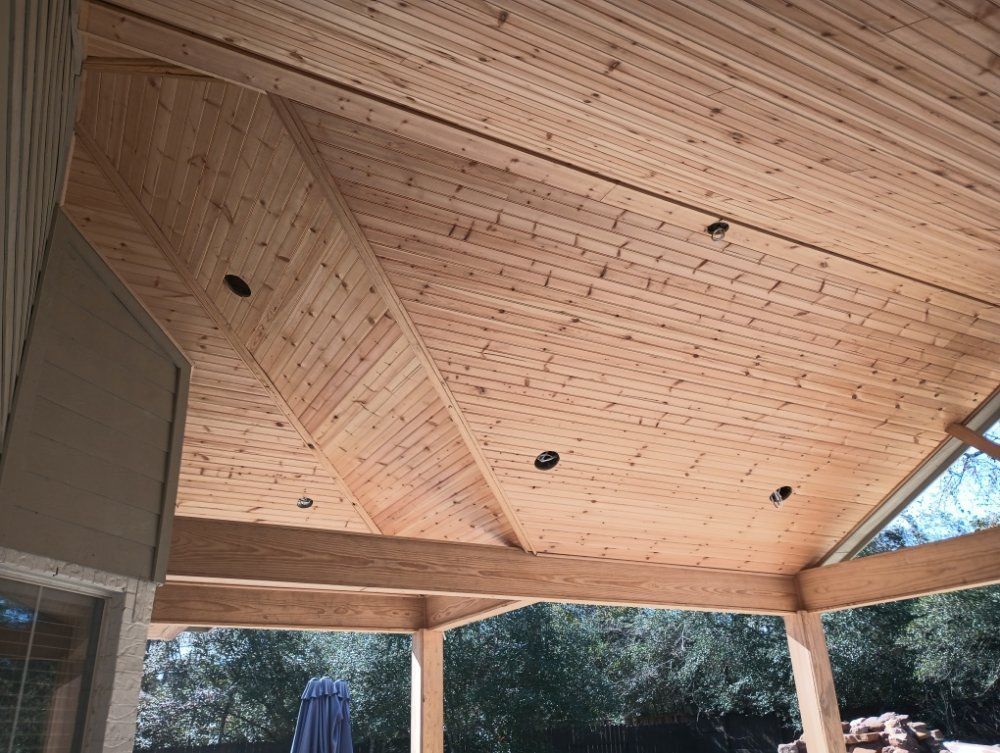 The ceiling of a wooden porch with a blue umbrella in the background.