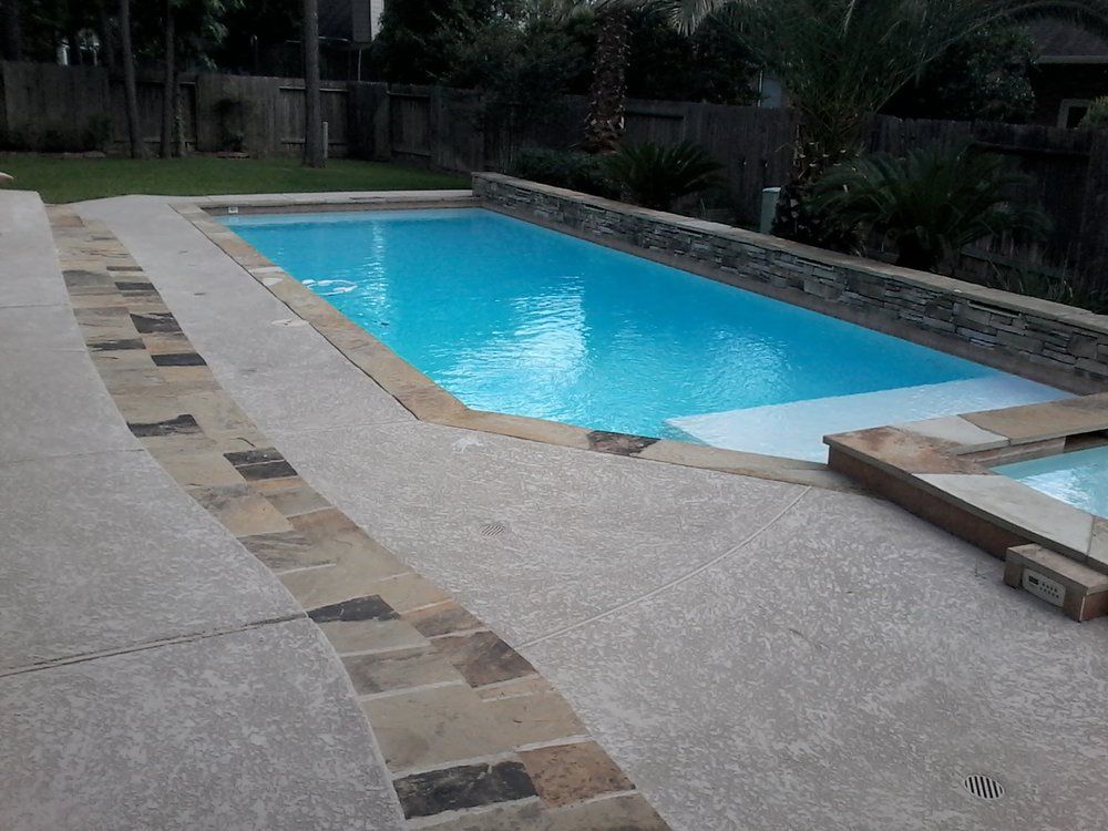 A large swimming pool in a backyard with a stone border