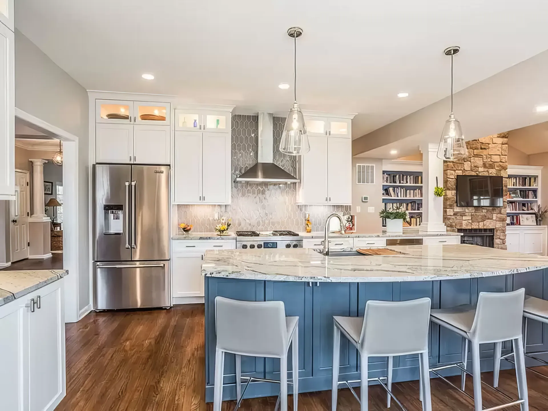 A kitchen with a large island , stools , a refrigerator , and a stove.
