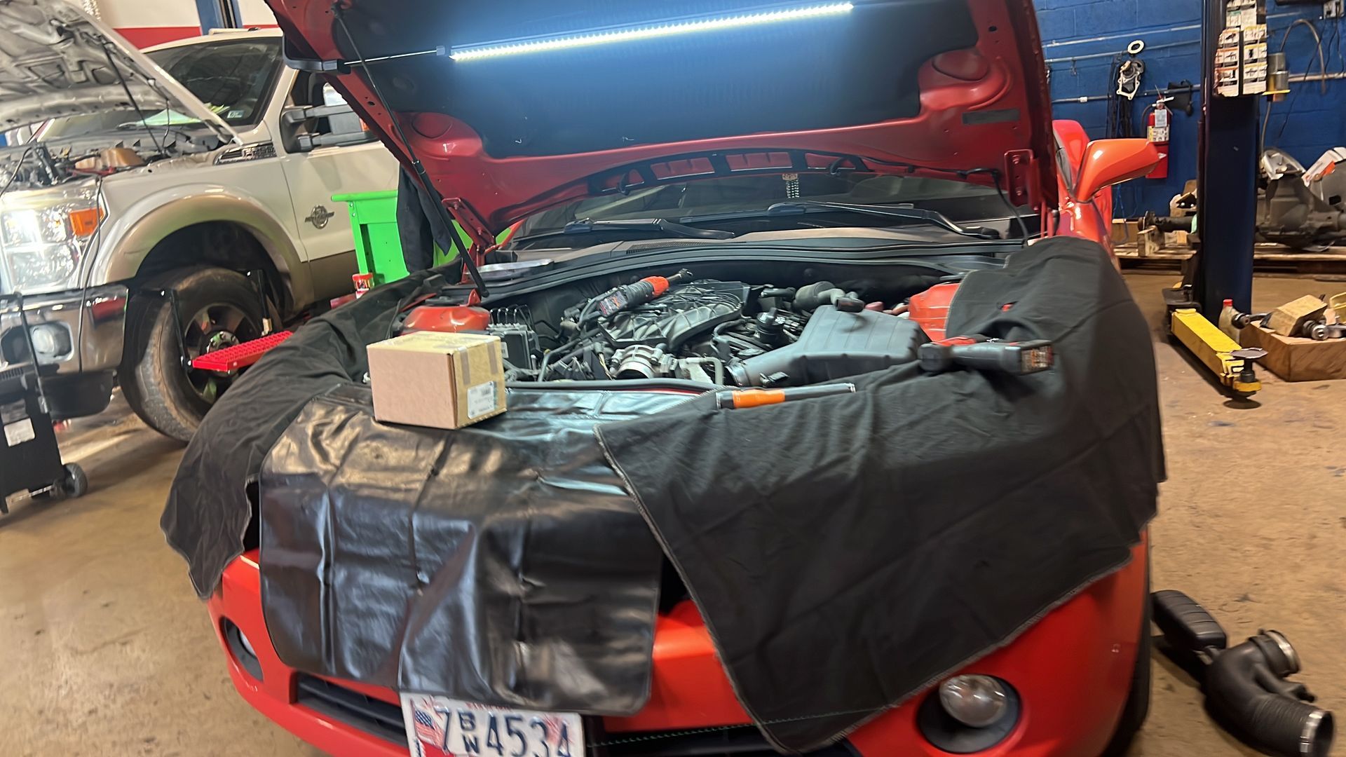 A red car with the hood up is being worked on in a garage.